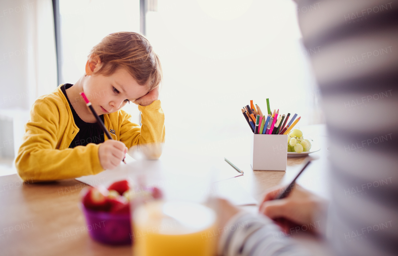 An unrecognizable mother with small daughter drawing pictures in a kitchen.
