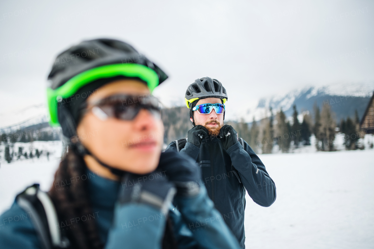 Group of mountain bikers standing on road outdoors in winter, fastening helmet.