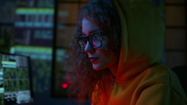 A young woman hacker by computer in the dark room at night, cyberwar concept.