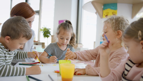 A group of small nursery school children with teacher indoors in classroom, painting.