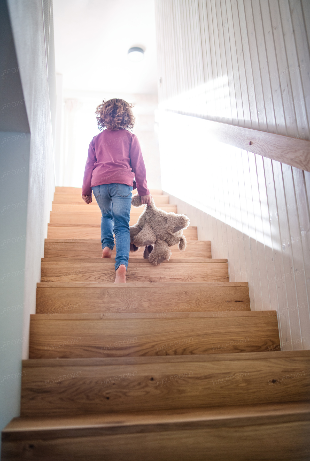 A rear view of small girl walking up wooden stairs indoors at home. Copy space.