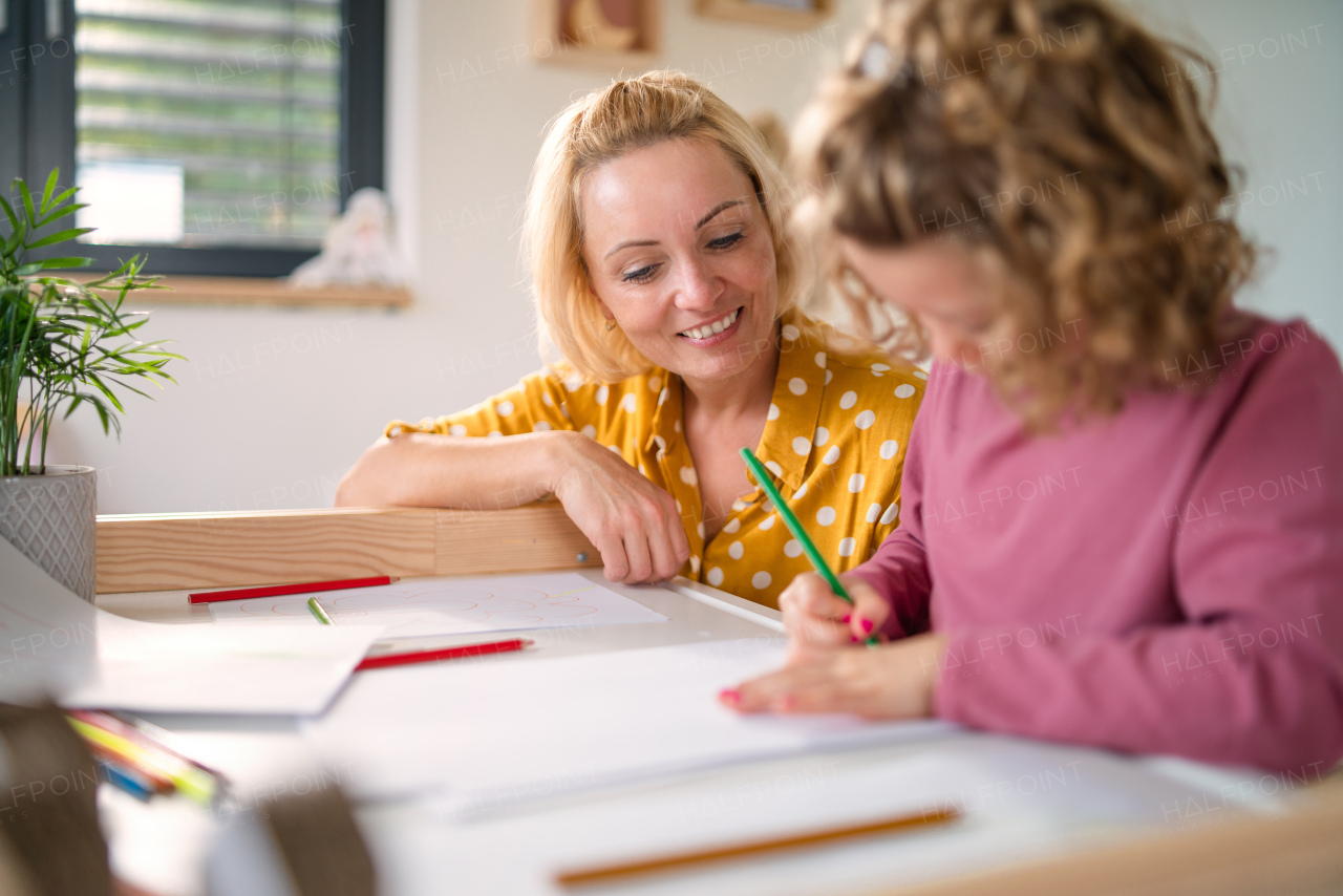 A cute small girl with mother in bedroom indoors at home, drawing pictures.