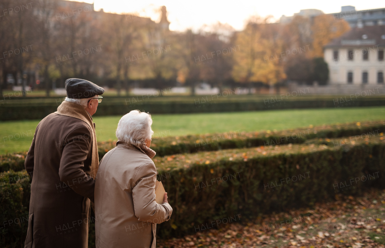 A happy senior couple on walk outdoors in town park in autumn.