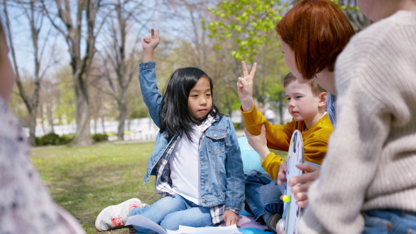 A teacher with small children sitting outdoors in city park, learning group education concept.