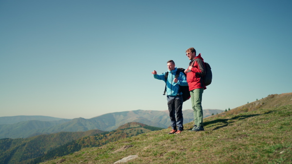 Paragliders walking up hill to paragliding starting point, on a sunny morning in mountains.