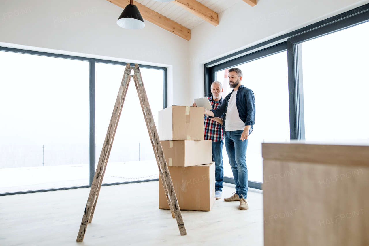 A cheerful senior man with tablet helping his mature son with furnishing new house, a new home concept.