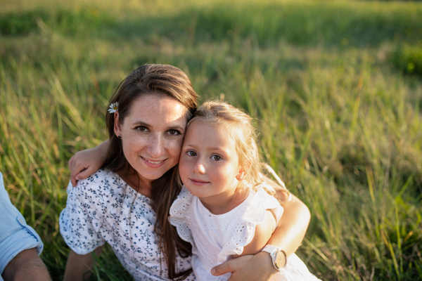 Mother with small toddler daughter on walk on meadow outdoors, looking at camera.