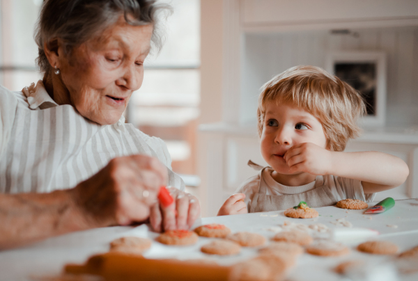 A senior grandmother with small toddler boy making and decorating cakes at home.