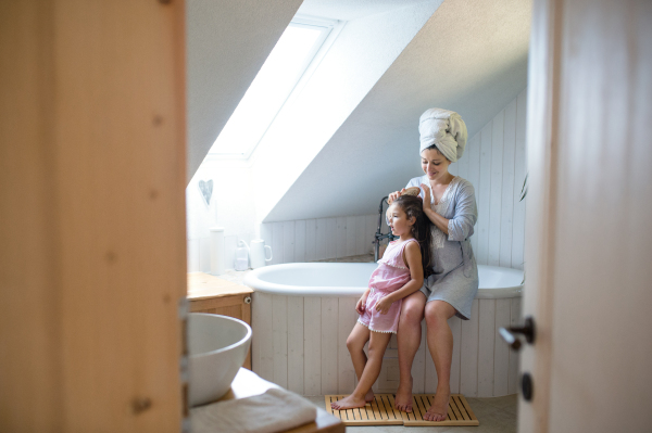 Side view portrait of pregnant woman with small daughter indoors in bathroom at home, brushing hair.