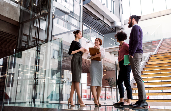 A group of young businesspeople standing near a staircase, talking.