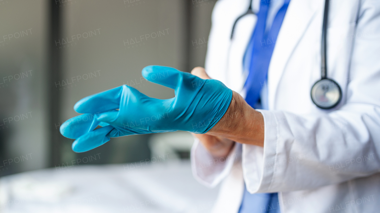 Midsection of unrecognizable senior woman doctor putting on gloves in hospital, coronavirus concept.