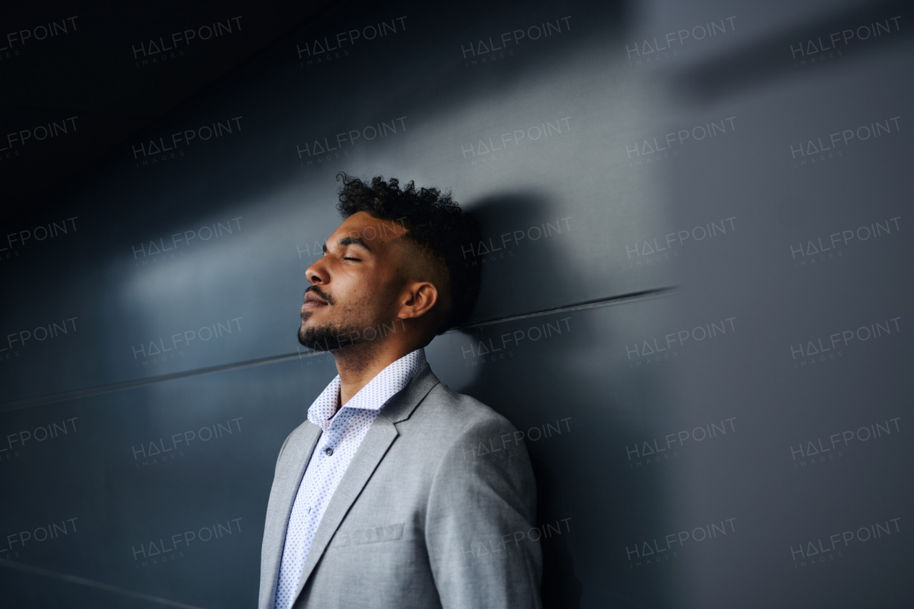 A portrait of young man student standing outdoors in city against black background, eyes closed.