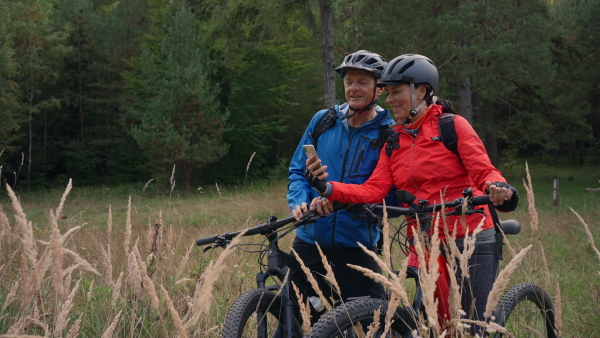 A senior couple bikers using smartphone outdoors in forest in autumn day.