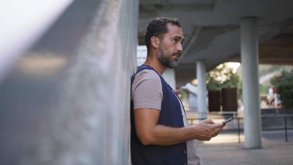A handsome mature man with smartphone waiting at station.