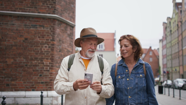 A happy senior couple tourists using smartphone outdoors in historic town