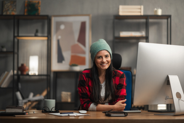 A happy female video editor works indoors in creative office studio, looking at camera.