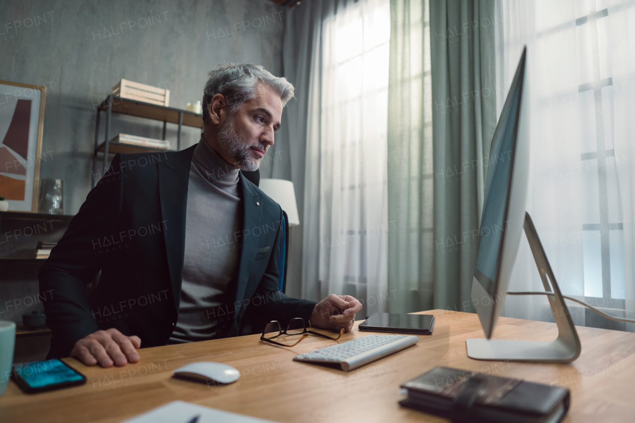 A mature businessman working on computer indoors in office.