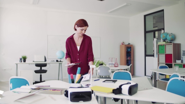 A teacher walking around desks in class, preparing for a lesson.