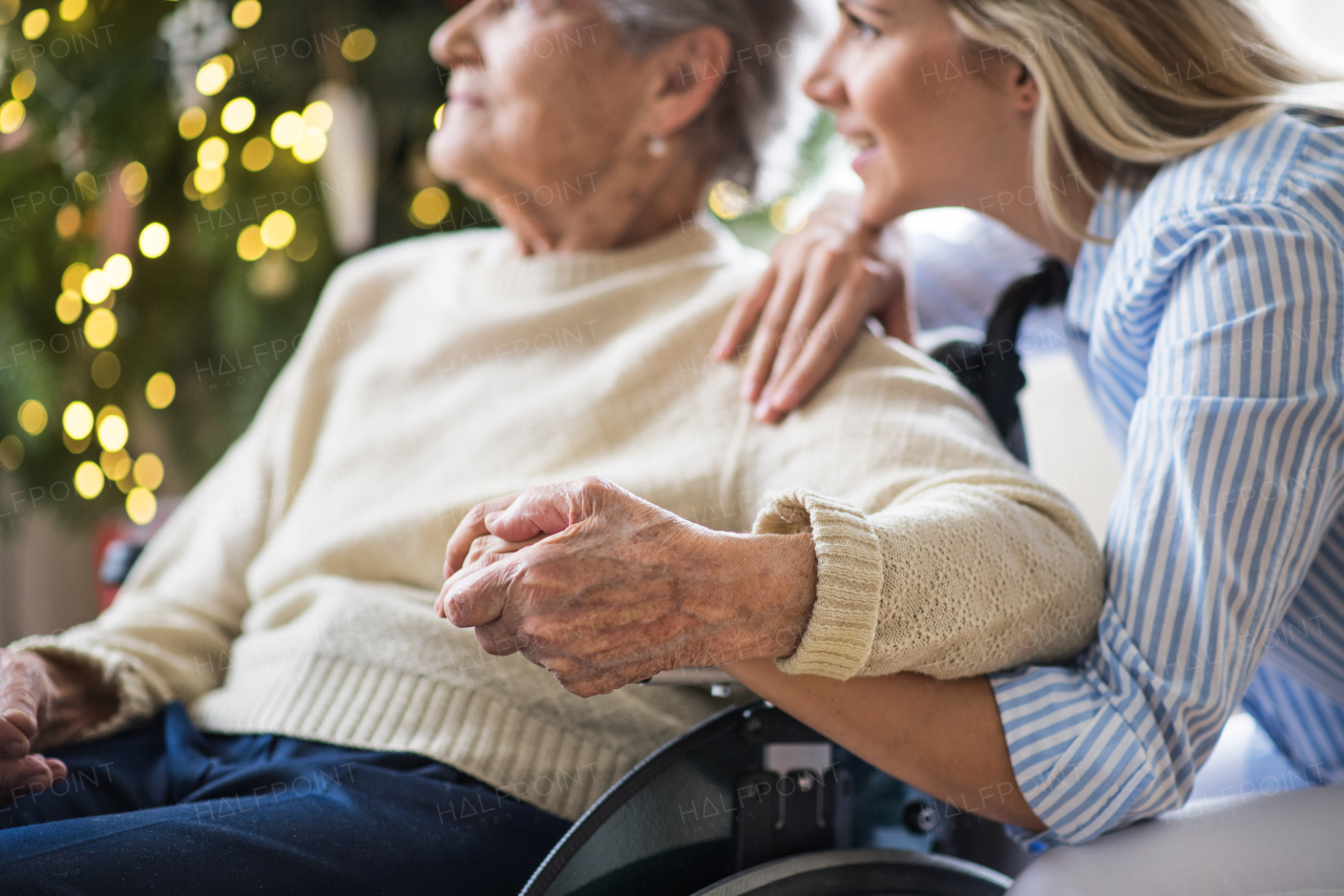 Unrecognizable senior woman in wheelchair with a health visitor at home at Christmas time, looking out of a window.