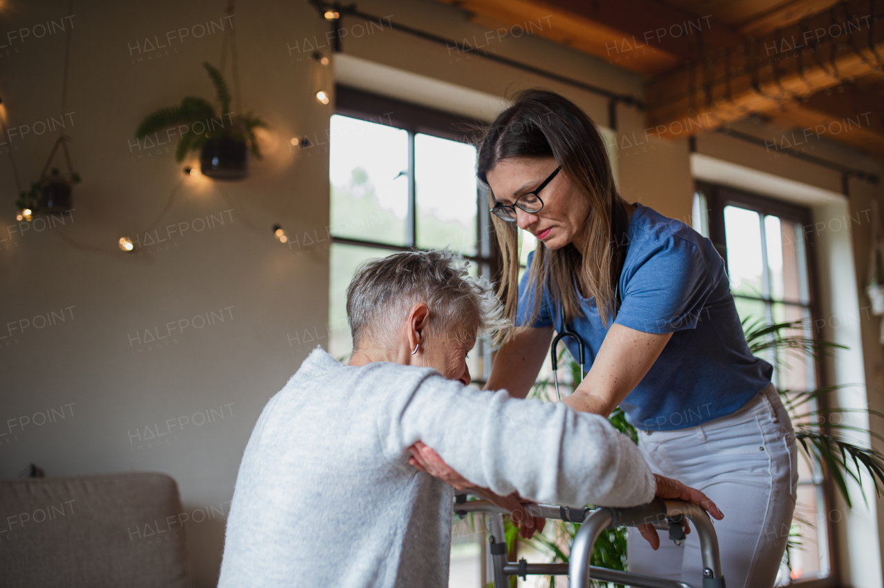 A healthcare worker or caregiver visiting senior woman indoors at home, helping her to walk.