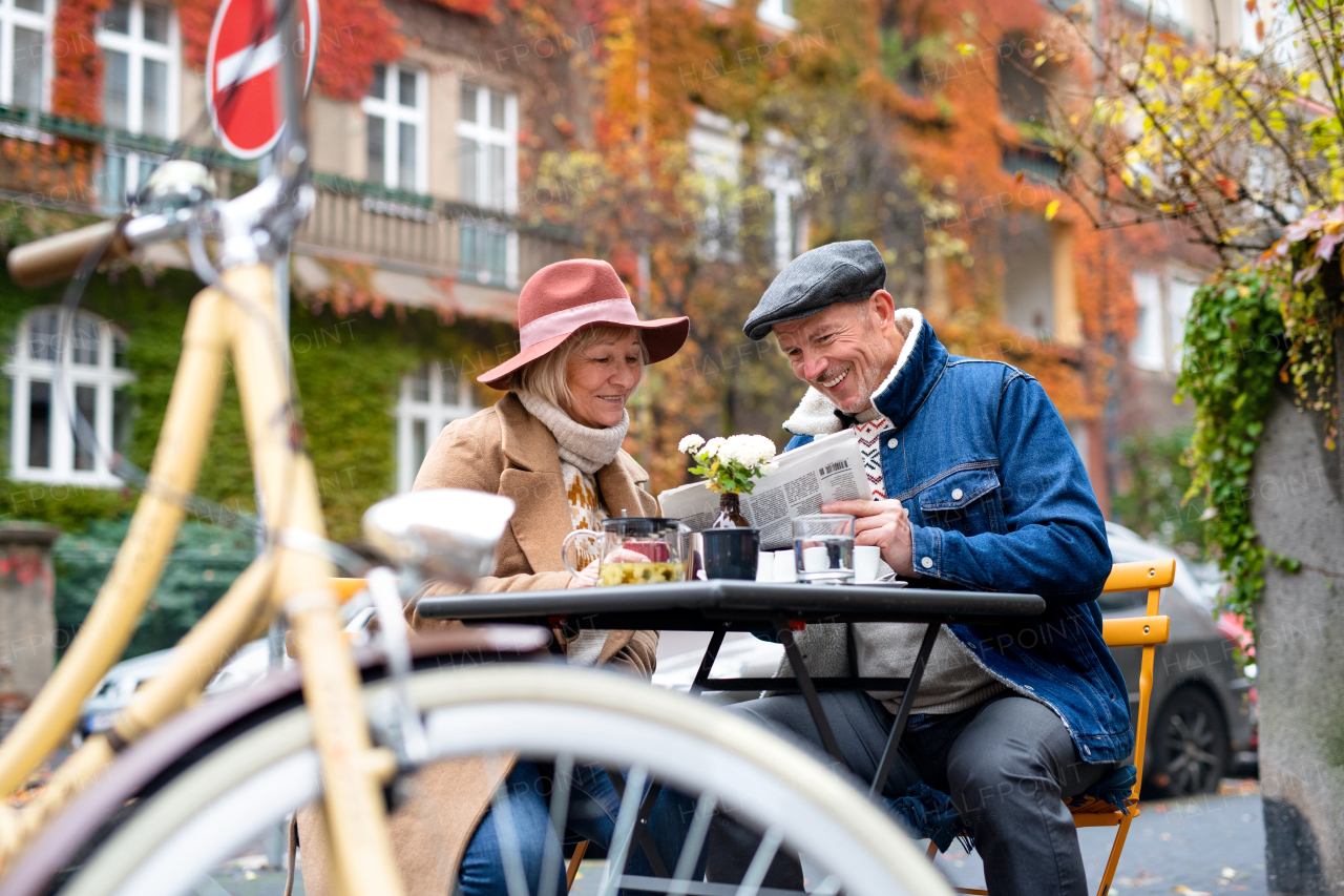 Happy senior people sitting in outdoor cafe in city, reading newspapers.