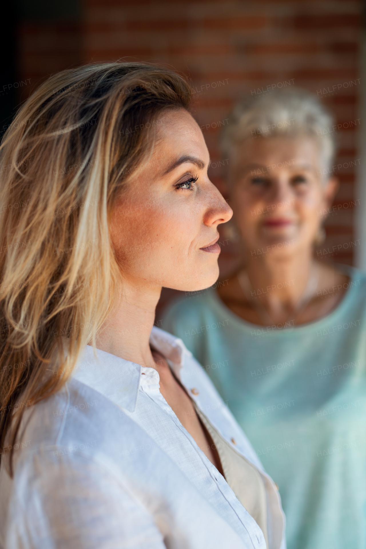 A senior mother looking at her adult daughter indoors at home. Selective focus on woman in foreground.