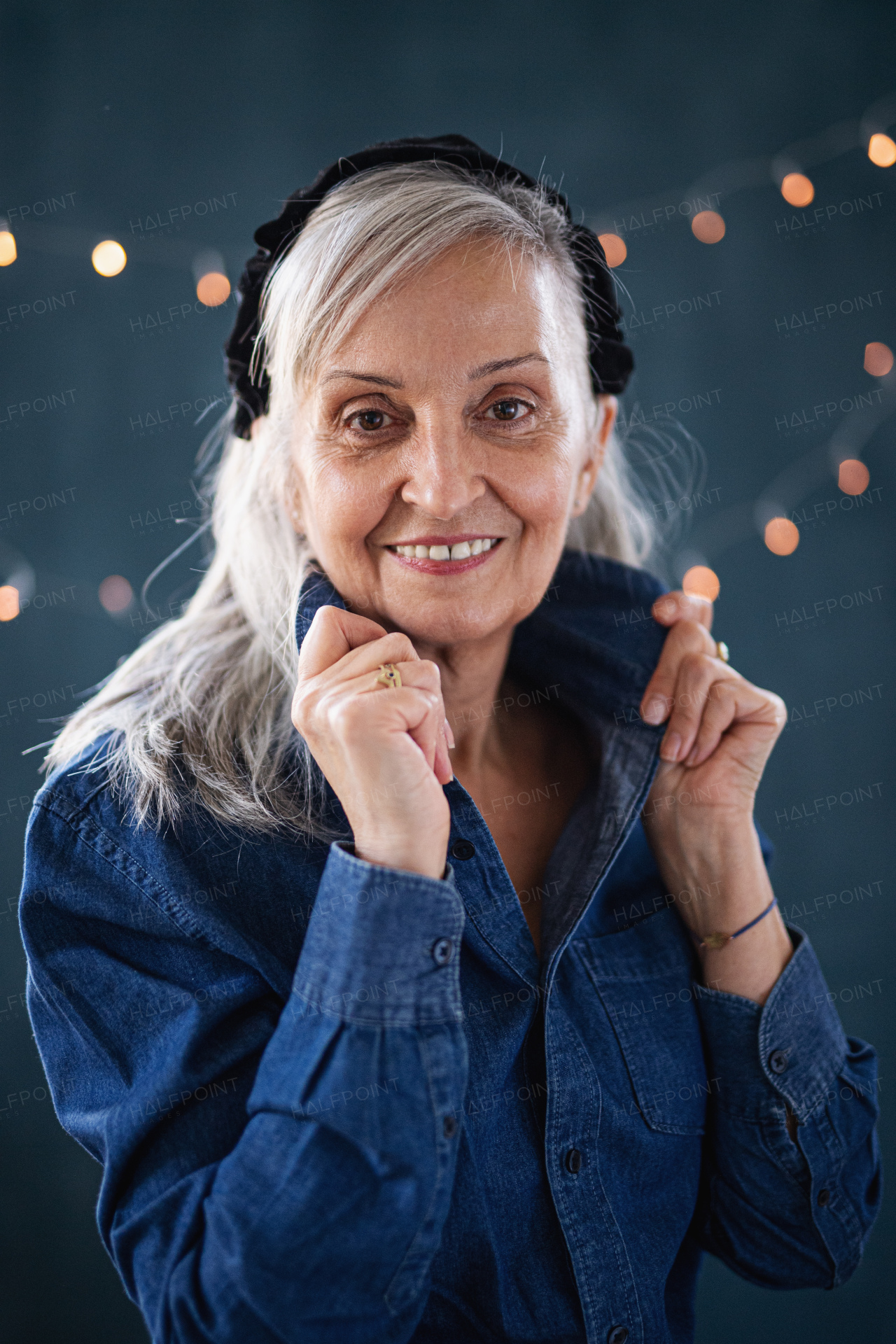 Front view portrait of senior woman standing indoors against dark background, looking at camera.