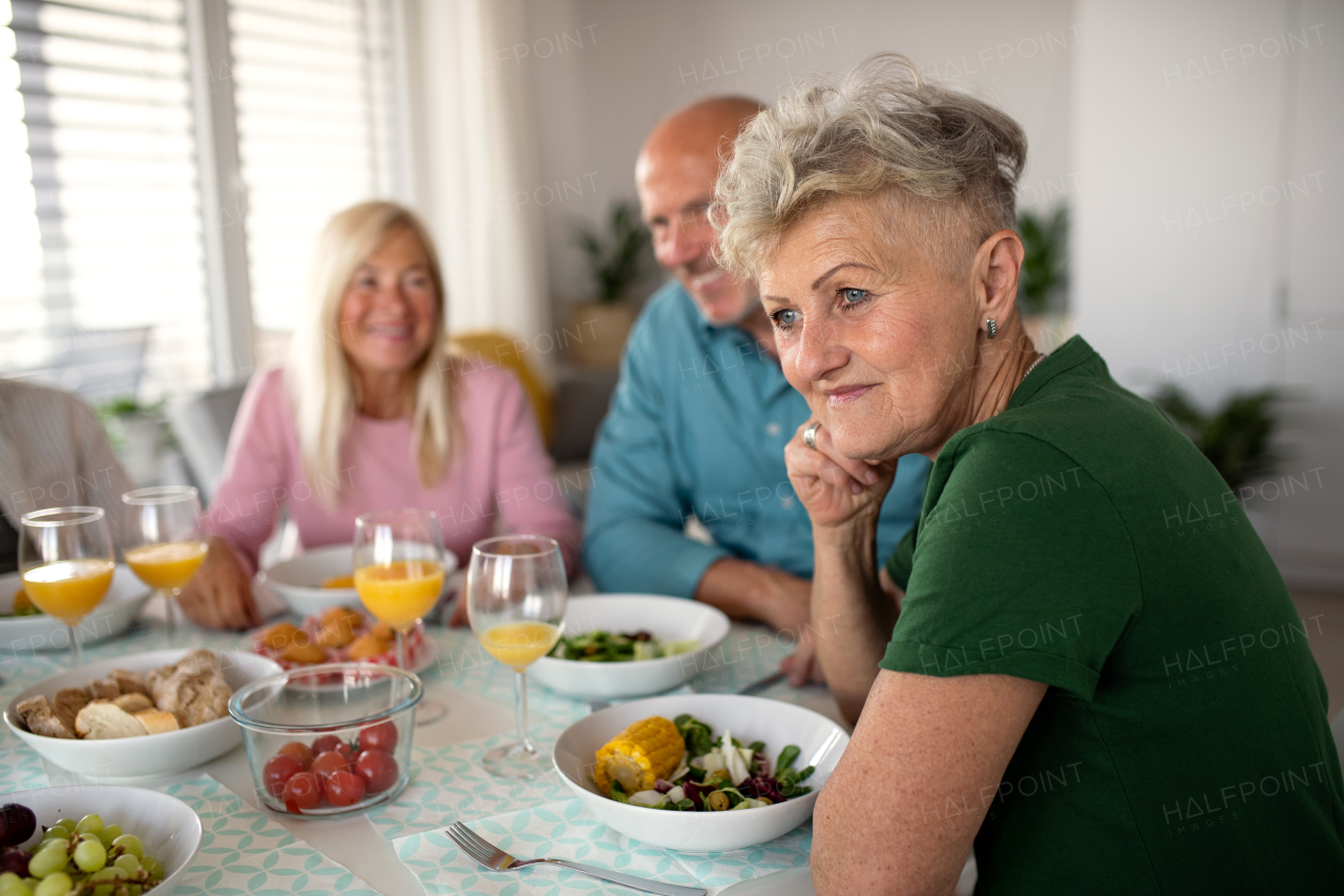 A senior woman with friends having party indoors, eating at the table.