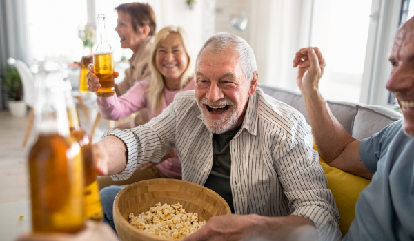 Group of cheerful senior friends watching movie indoors, party, social gathering and having fun concept.