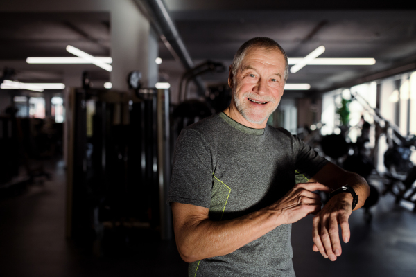 A cheerful senior man with smartwatch in gym measuring time while doing exercise. Copy space.
