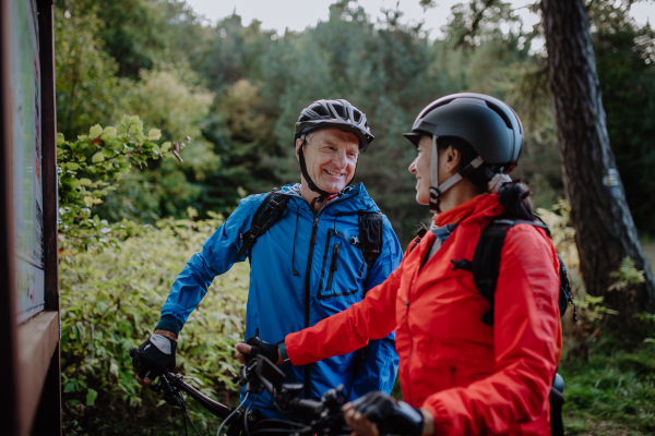 A happy senior couple bikers talking by map outdoors in nature in autumn day.
