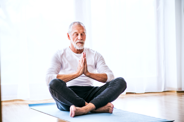Active senior man meditating at home, eyes closed.