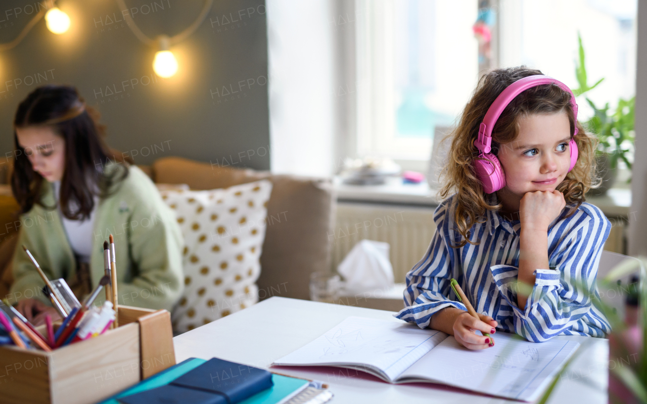 Portrait of sisters schoolgirls learning online indoors at home, coronavirus concept.