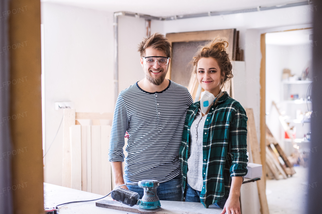 Small business of a young couple. Man and woman worker with a sander in the carpenter workroom.