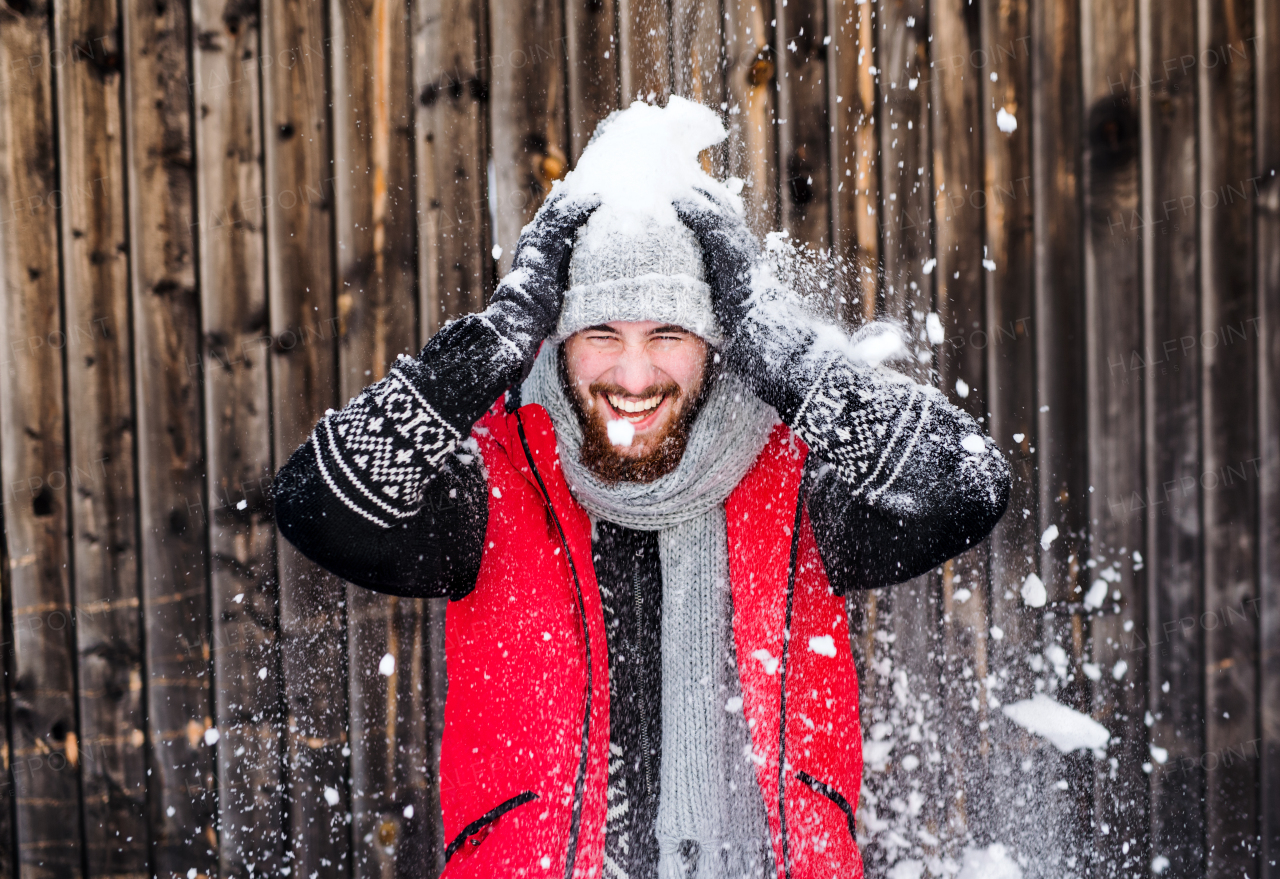 Front view portrait of young man standing against wooden background outdoors in winter, having fun.