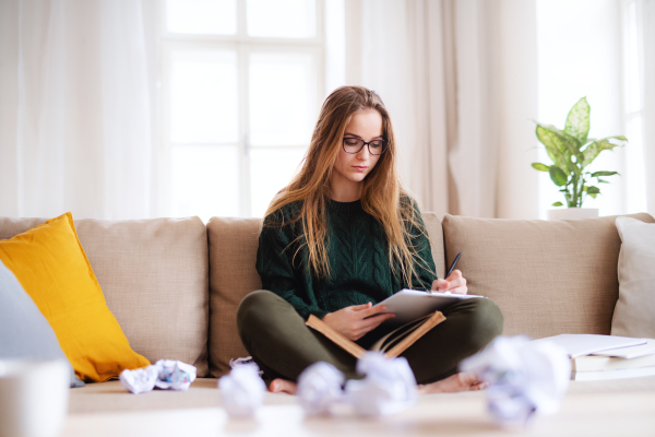A happy young female student sitting on sofa, studying. Copy space.