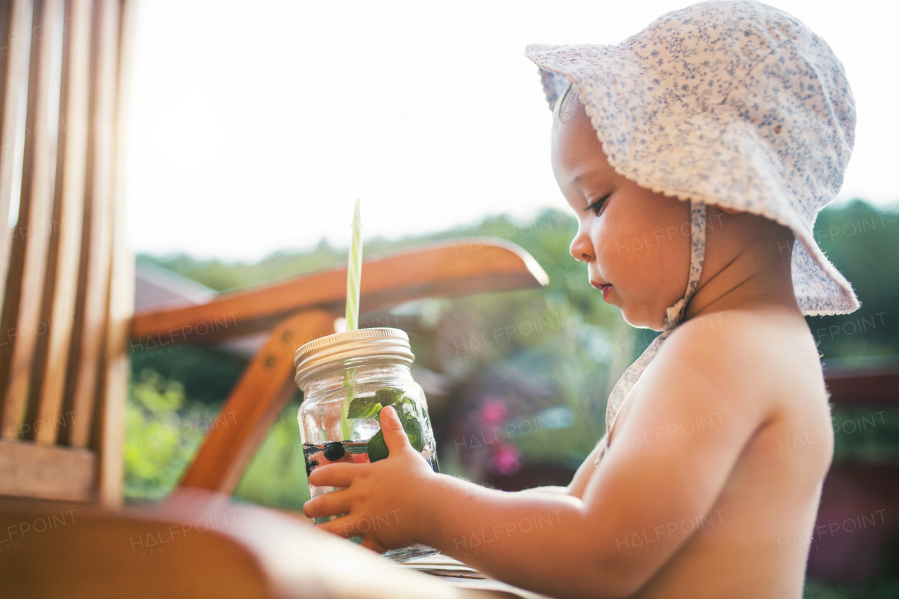 A small girl with a drink with fruit standing by a table on a patio in summer.