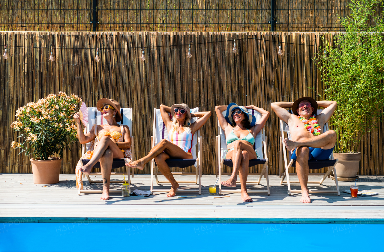 Group of cheerful seniors sitting by swimming pool outdoors in backyard, relaxing.
