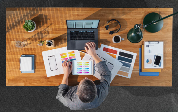 A top view of businessman working on laptop computer at desk with paperwork in home office.