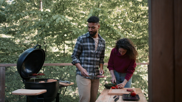 A happy couple resting and preparing burgers outdoors in a tree house, weekend away and digital detox concept.