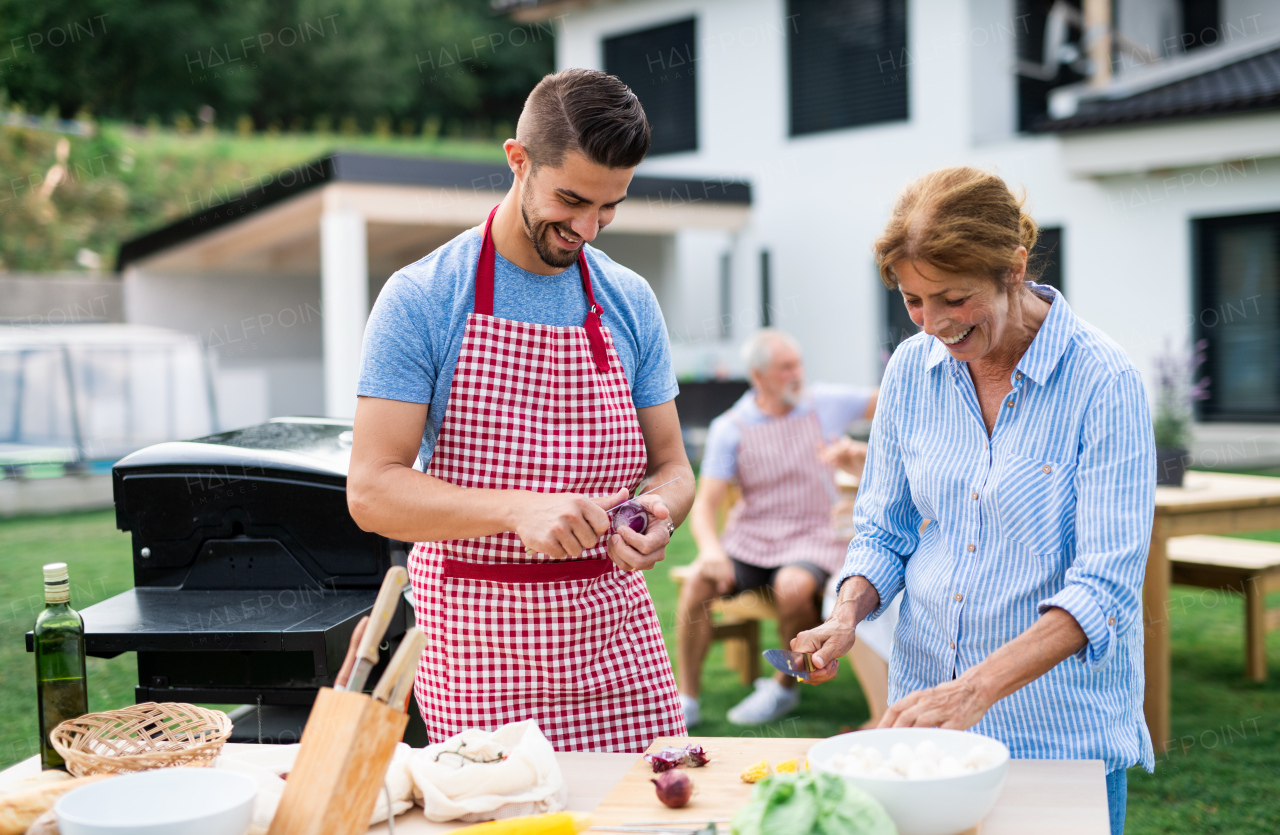Portrait of multigeneration family outdoors on garden barbecue, grilling and talking.