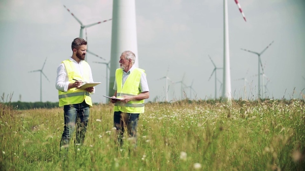 Two engineers or technicians with clipboard standing on wind farm, making notes. Slow motion.