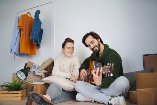 Happy young couple with boxes and guitar moving in new flat, new home and relocation concept.