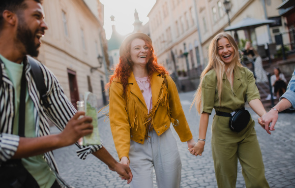 Front view of group of laughing young people outdoors on street on town trip, walking and holding hands.