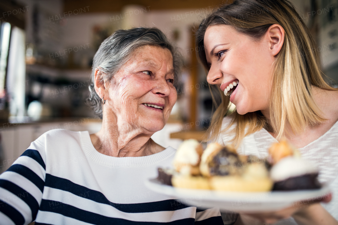 Portrait of an elderly grandmother with an adult granddaughter at home. Women sitting at the table, holding a plate full of cakes.