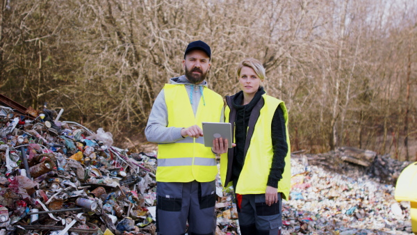 Man and woman workers with tablet on landfill, waste management and environmental concept.