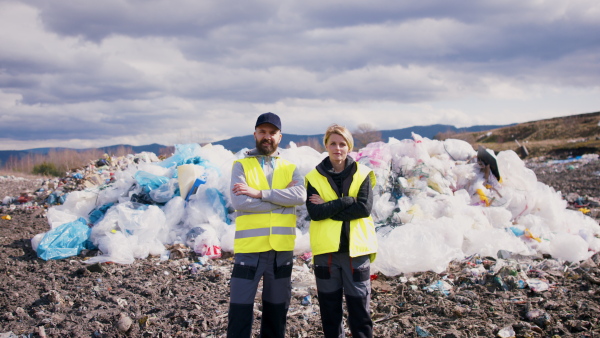 Man and woman workers standing on landfill, waste management and environmental concept.
