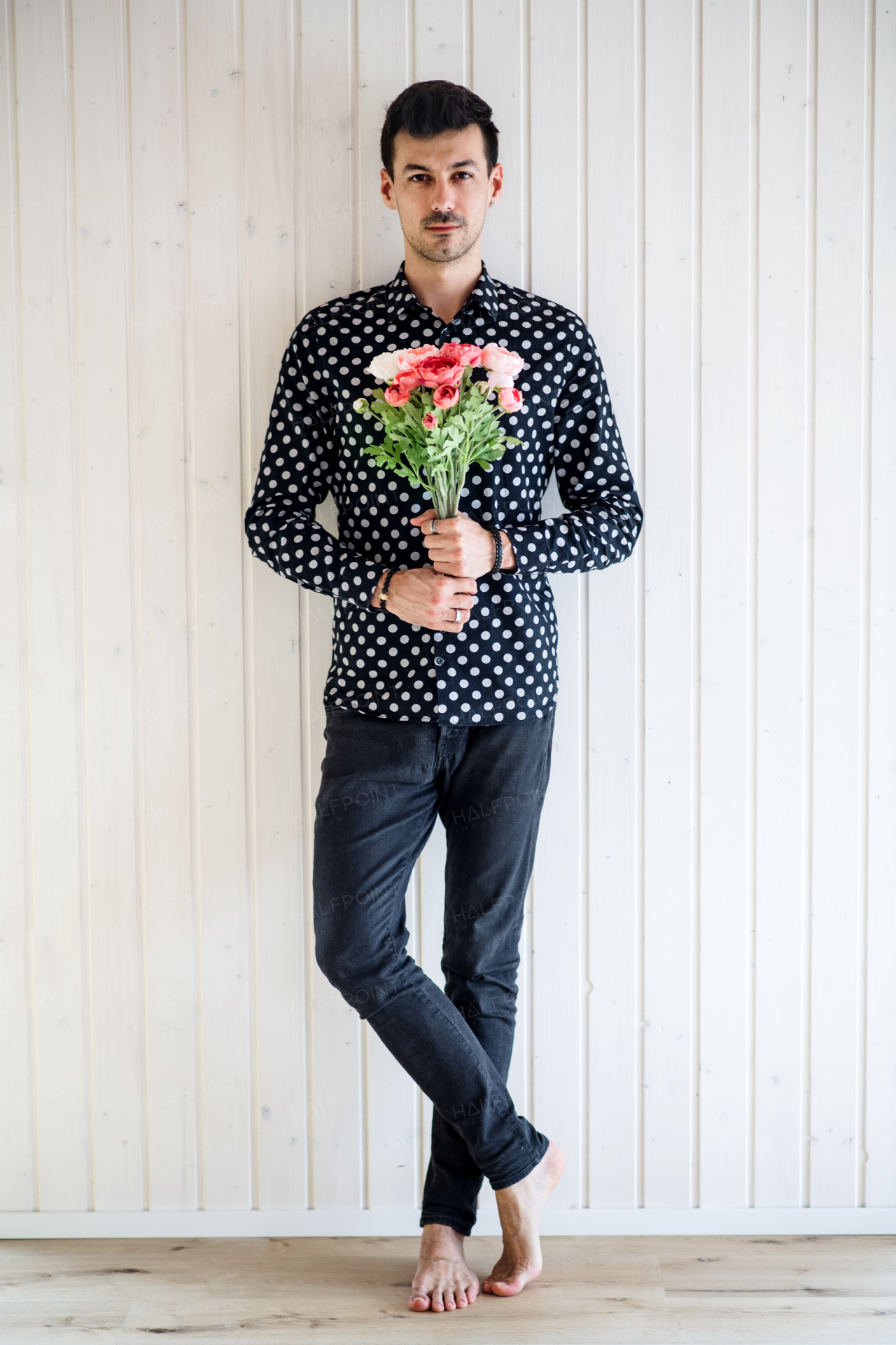 Handsome young man with flowers standing against white wooden background wall.