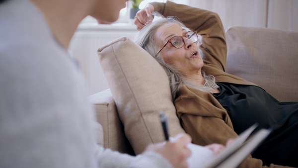 Sad senior woman talking to unrecognizable therapist indoors, mental health concept.
