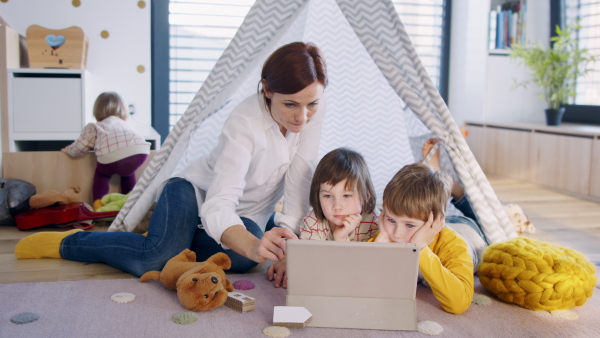 Front view of mother with small children in bedroom at home, using tablet.
